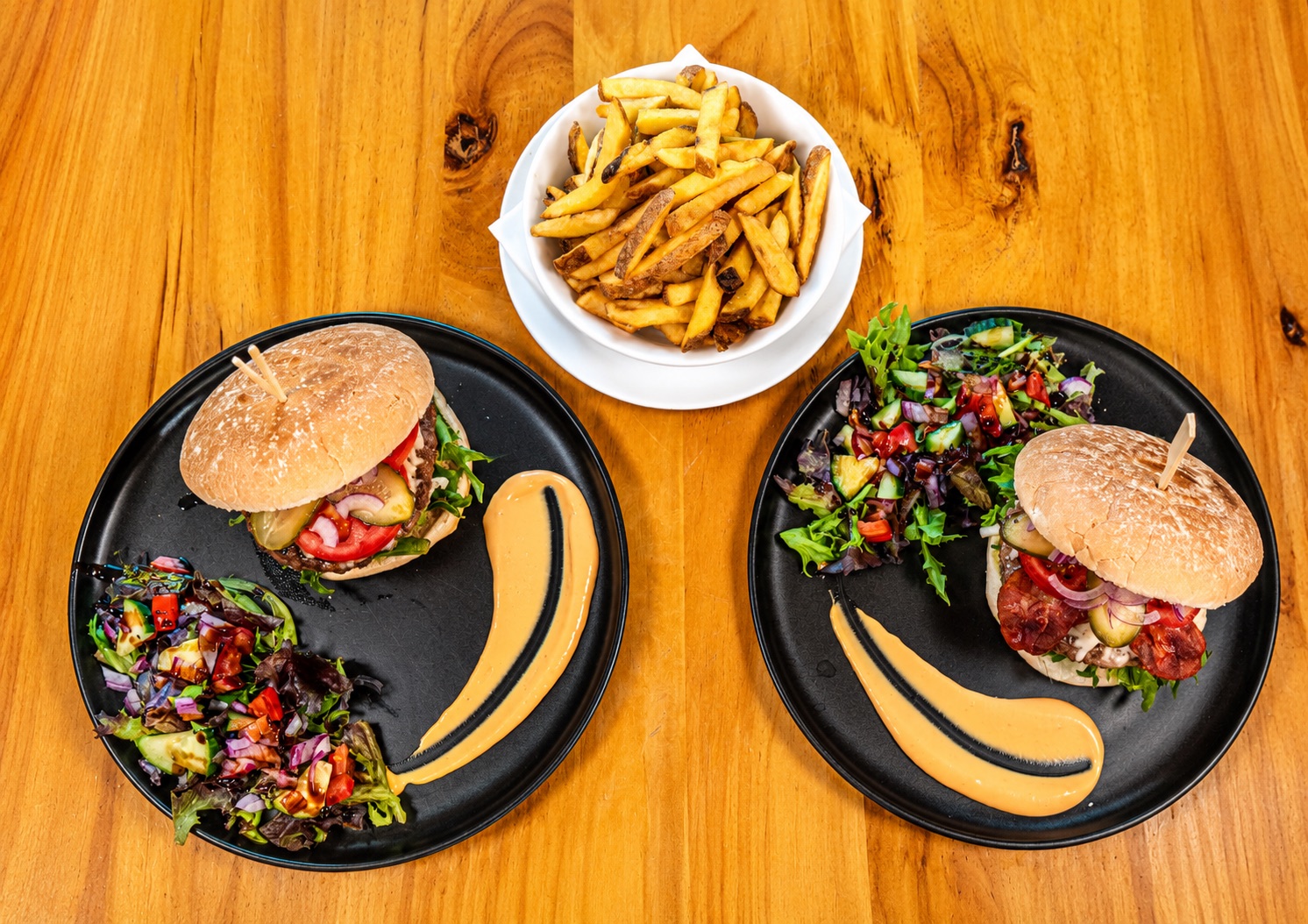 Two burgers with salad and a bowl of chips on a wooden table at Heaven Coffee Shop.